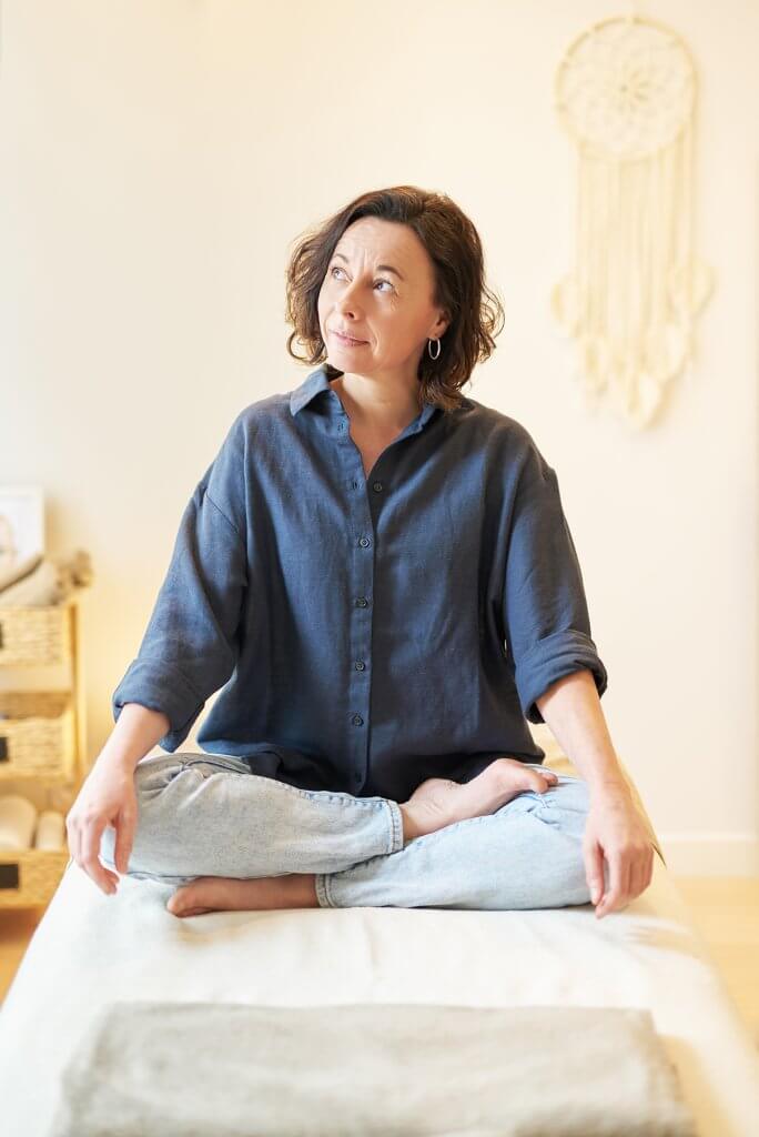 Portrait d’une masseuse assise sur table de soin dans un studio de massage cocooning et apaisant