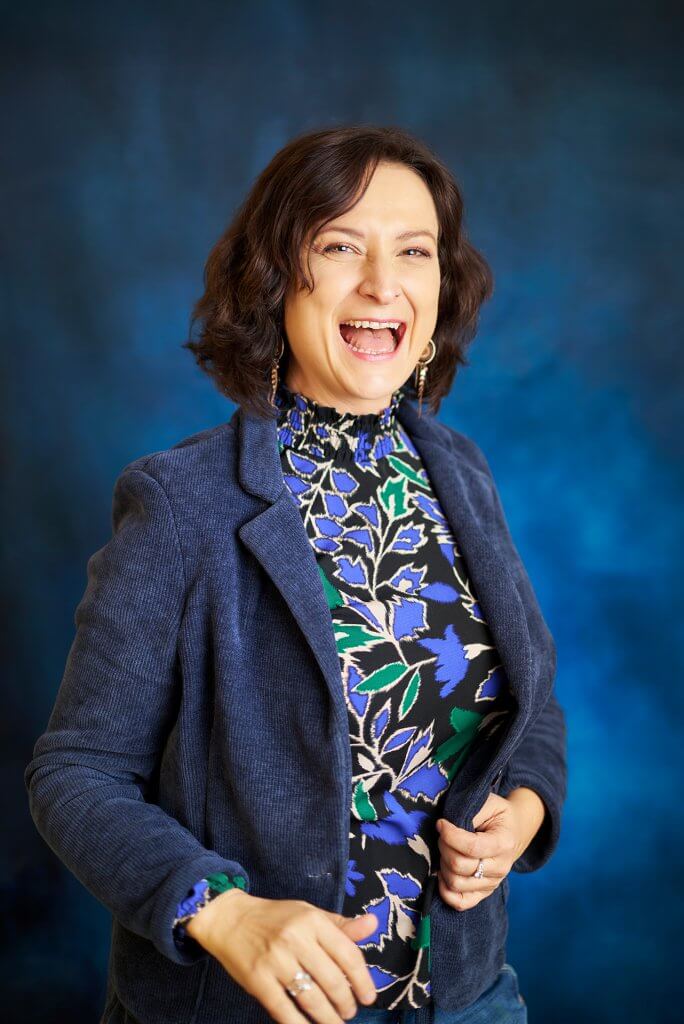 Entrepreneure du domaine du développement personnel éclatant de rire sur fond bleu marine lors d’un shooting corporate.
