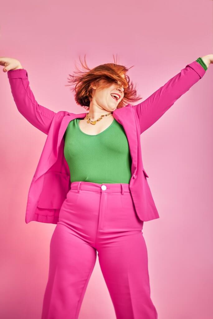 Coach en costume rose exprimant sa joie sur un fond rose vif