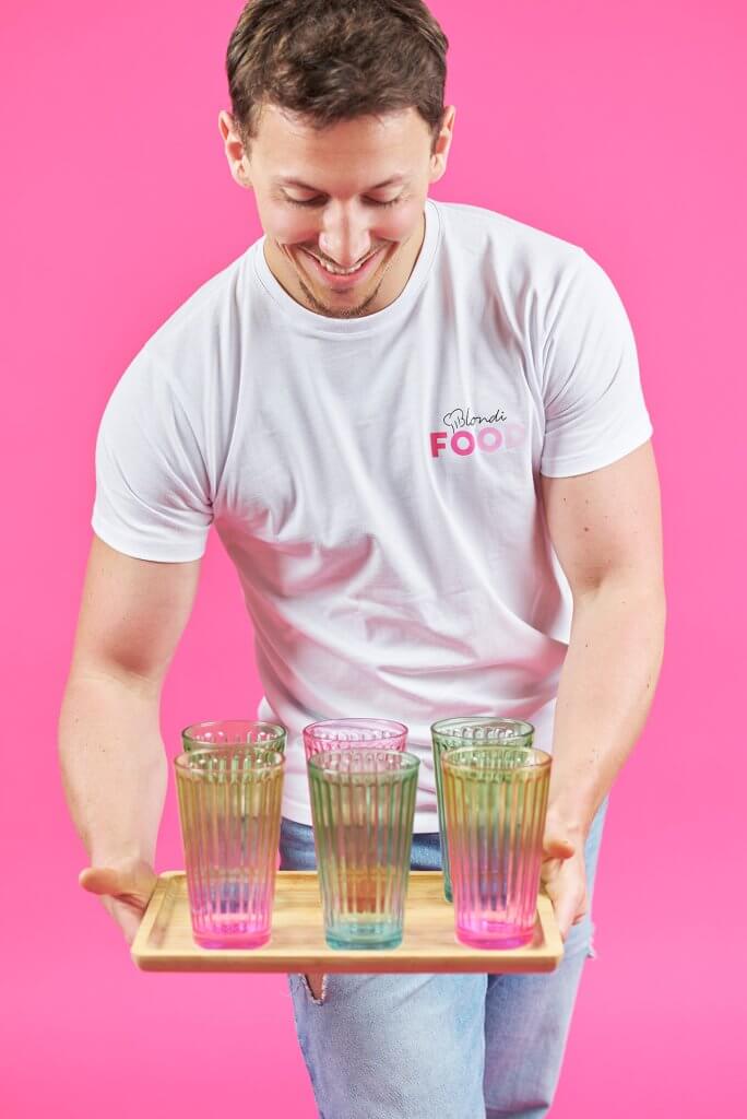 Gérant portant un plateau de boissons colorées dans un univers rose pop