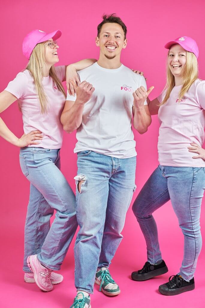 Équipe BlondiFOOD riant ensemble sur fond rose pendant un shooting corporate