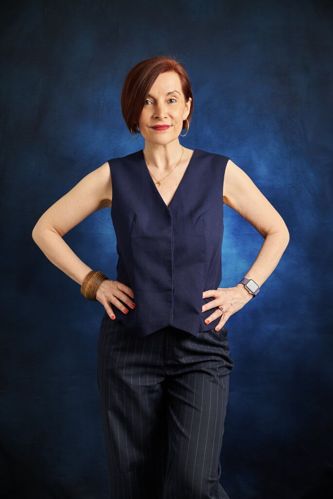 Portrait corporate femme monochrome sur fond bleu avec tenue bleu, mains sur les hanches et souriante