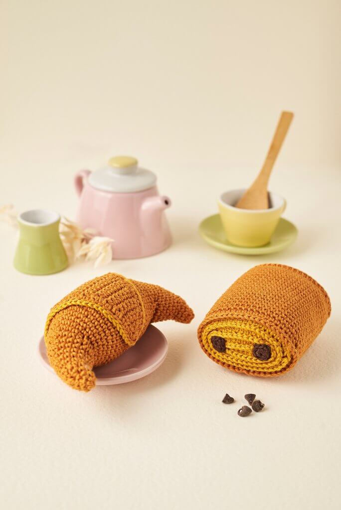 Petit pain au chocolat et croissant au crochet mis en scène avec dinette pastel sur fond crème