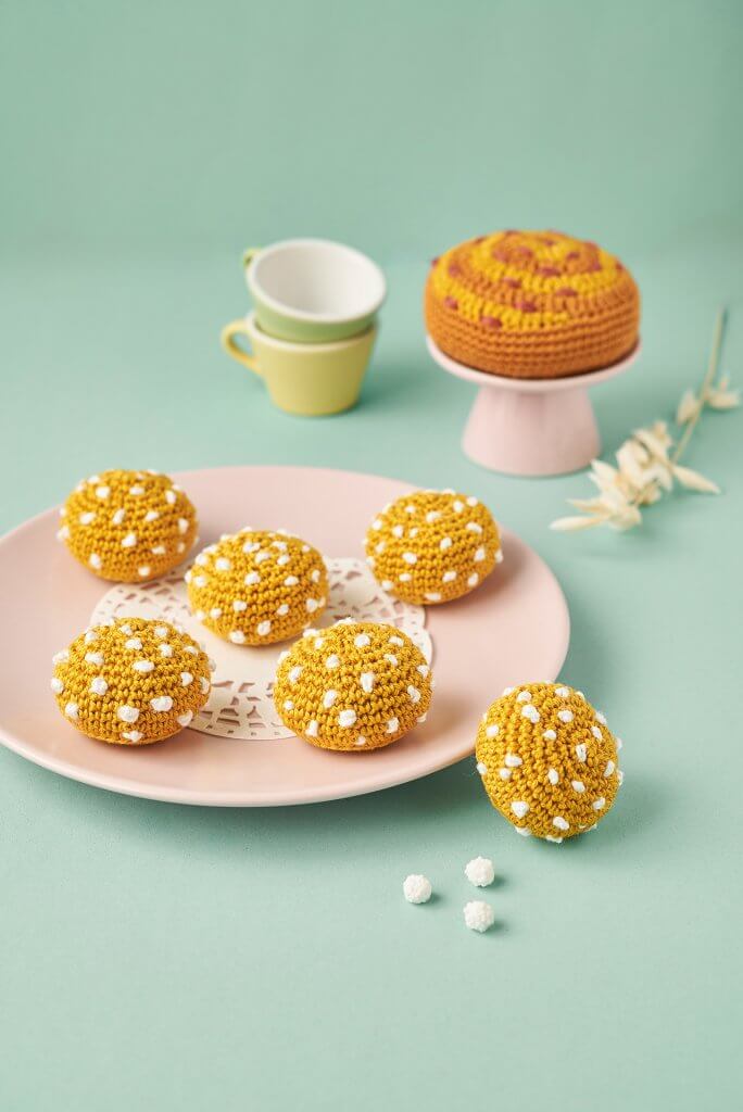Chouquettes au crochet disposées dans assiette rose sur fond turquoise accompagnée de dinette