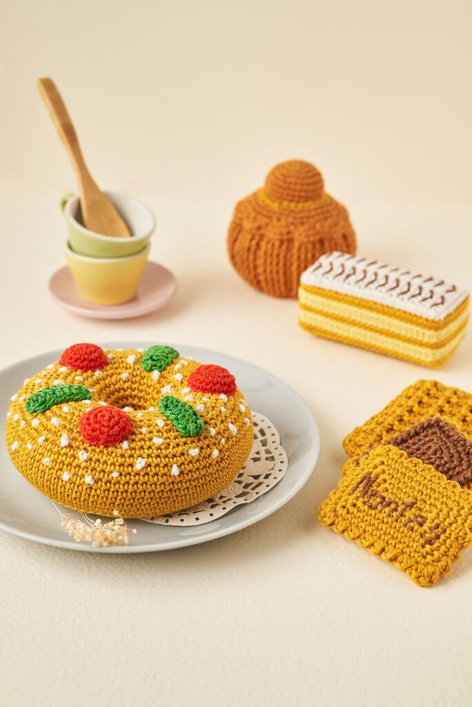 Gâteaux au crochet mis en scène dans dinette pastel sur fond ivoire